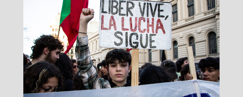 IMagen de estudiante con puño en alto durante la marcha de mártires estudiantiles, con cartel que dice: "Liber vive, la lucha sigue"